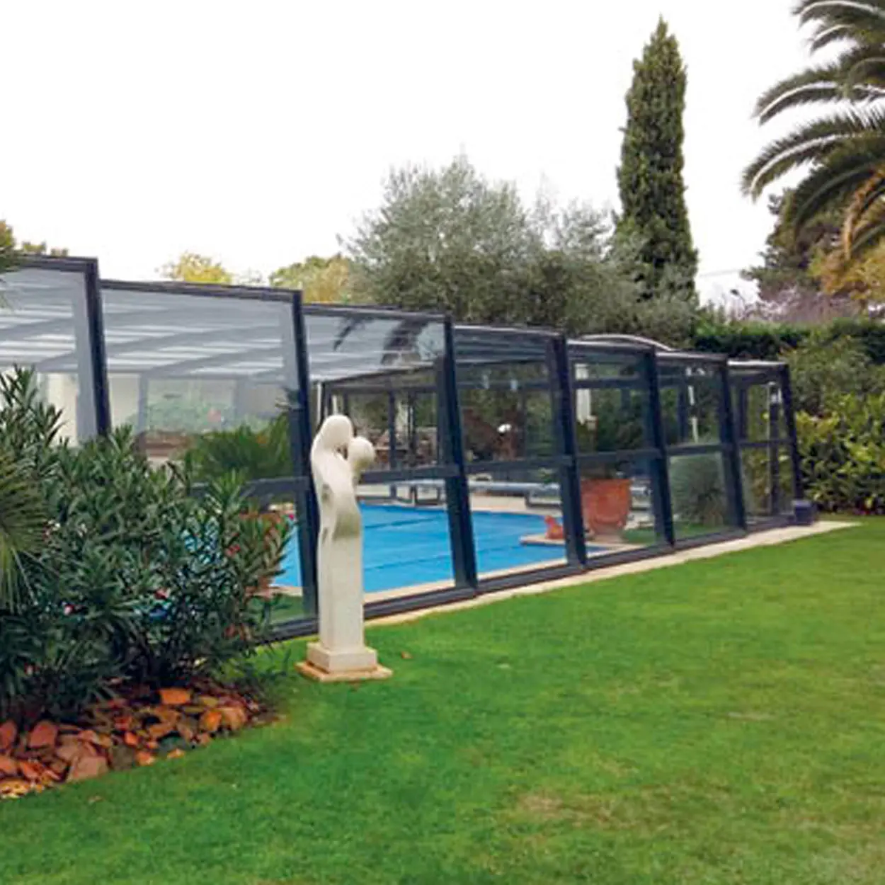 Piscine entourée d'un abri haut vitré sécurisé dans un jardin paysager