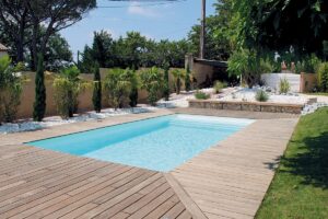 Piscine en béton rectangulaire avec terrasse bois dans un jardin paysager du Morbihan