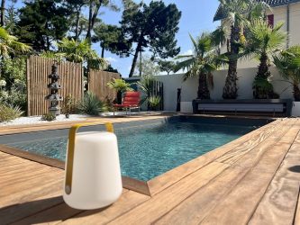 Lampe LED outdoor posée sur une terrasse en bois au bord d'une piscine design avec palmiers